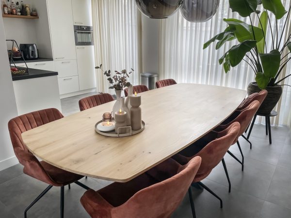 Eetkamer met massief eiken deens ovaal tafelblad en zwarte matrixpoot. Op de tafel staat wat decoratie en aan de tafel staan 8 kuipstoelen in koper kleur