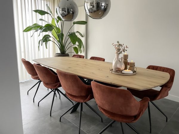 Eetkamer met massief eiken deens ovaal tafelblad en zwarte matrixpoot. Op de tafel staat wat decoratie en aan de tafel staan 8 kuipstoelen in koper kleur