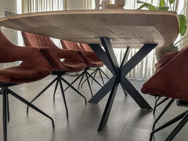 onderkant van het deens ovaal massief eiken tafelblad, waarbij je de verjongde randen goed ziet. Het blad is gemonteerd op een zwart stalen matrispoot en er staan koperkleurige stoelen aan de tafel