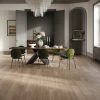 Ruime eetkamer met een eettafel en stoelen. Aan het plafond hangt een kristallen kroonluchter. Op de achtergrond zie je openslaande deuren naar de volgende ruimte. er ligt een mooie natuurlijk bruin/grijze laminaatvloer met waterbestendige toplaag van Parador in de ruimte. Type Parador Hydron 600, eiken skyline parelgrijs. In de gebruiksklassen van laminaat valt deze vloer onder klasse 32